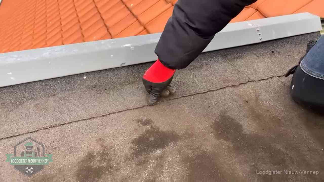 Vakman wijst een naad met vochtplekken aan op een bitumen plat dak in Nieuw-Vennep