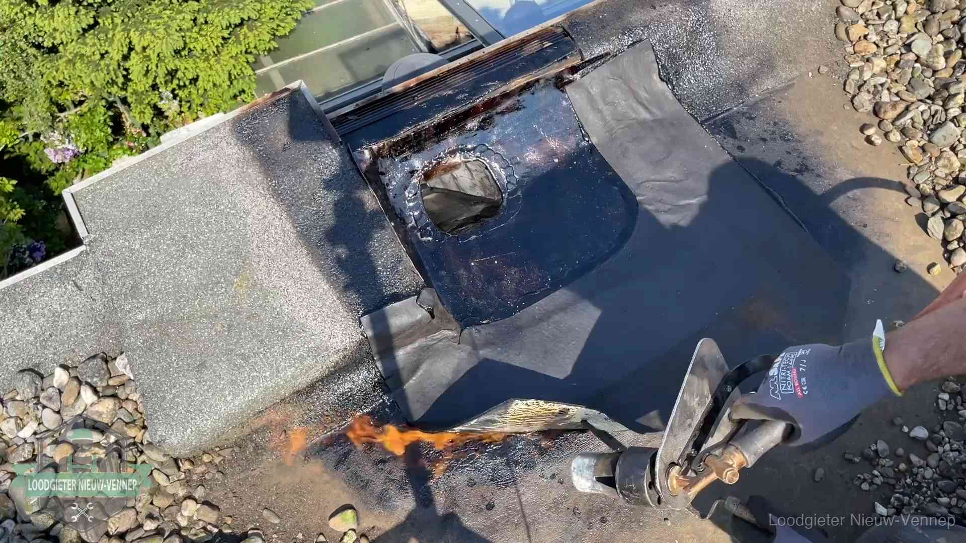 Dakdekker brandt bitumen rond een doorvoer tijdens een daklekkage-reparatie in Nieuw-Vennep