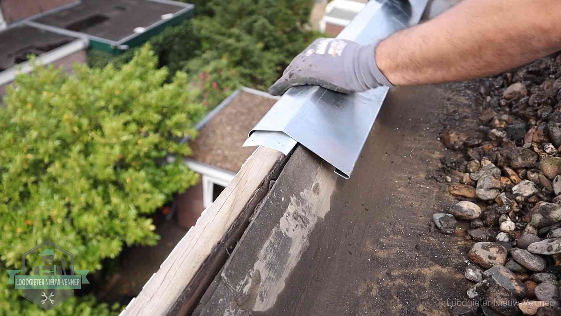 Dakdekker plaatst een zinken deklijst op een dakrand met uitzicht over een woonwijk in Nieuw-Vennep