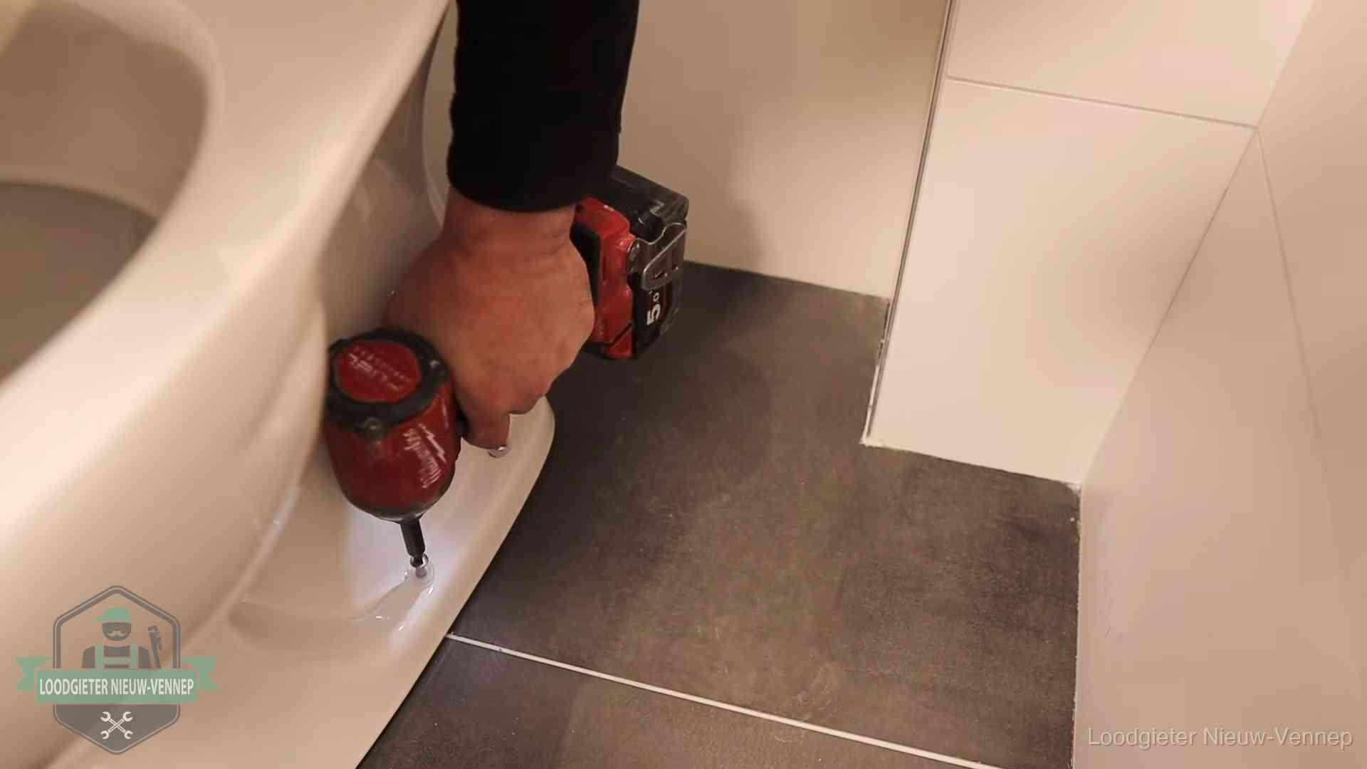 Loodgieter zet de voet van een wc-pot vast op de tegelvloer in Nieuw-Vennep
